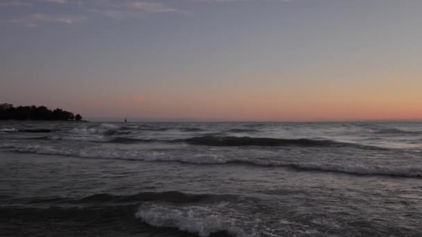 Clipe de movimento lento de ondas rolando na costa e batendo um no outro e salpicando na distância no início da manhã como o céu começa a se tornar rosa . — Vídeo de Stock