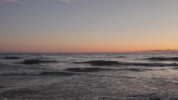 Yavaş çekim, Michigan Gölü üzerinde gün doğumunun görüntüsü. Bulutlar pembe ve turuncu renge bürünüyor. Dalgalar kıyı şeridine doğru yuvarlanıyor.. — Stok video
