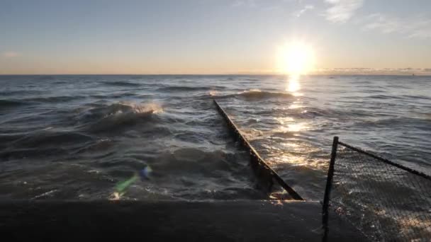 Långsam havsbild klipp av solen reflekterar på vattnet och våt betong strandlinje barriär som vågor kraschar, kolliderar och stänk i en korrugerad stålplåt högen och varandra. — Stockvideo