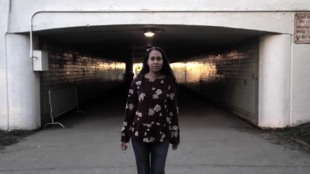 낙관적 인 인종인 아프리카 계 미국인 여성 이 어두운 지하 통로에서 도시 환경에서 가까운 거리로 카메라를 향해 걸어오는 느린 모션 클립. — 비디오