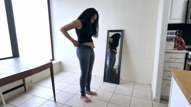 Mulher e mãe afro-americana bonita fica na frente de um espelho e tenta fechar sua calça jeans azul encaixe apertado após a dieta pós-parto e exercício de perda de peso . — Vídeo de Stock