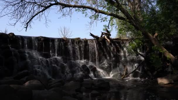 岩の多い崖の端から下の川に水が流れ落ち 上の湖の上に木が吊るされた静止したビデオ — ストック動画