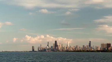 Gün batımında Chicago 'nun ufuk çizgisi yolculuğunun tarihi sona ererken yelkenliler mavi sularda ve Michigan Gölü' nün dalgalarında pembe ve mavi renkli bulutlarla gökdelen merkezindeki gökdelen yüksek binaların üzerinde ilerliyorlar..
