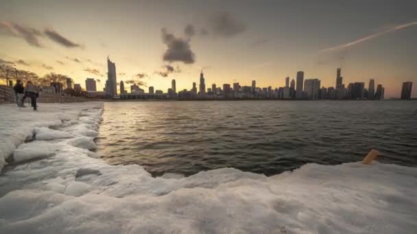 シカゴ 2019年3月10日 人々はプラネタリウム近くの雪と氷に覆われた海岸線に沿って集まり 都市のスカイラインの後ろの夕日を雲が頭上に浮かぶのを見る — ストック動画