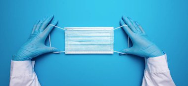 Doctor Hands in gloves showing medical face mask on blue background. Preventive measures to protect against Covid-19 Corona virus infection.