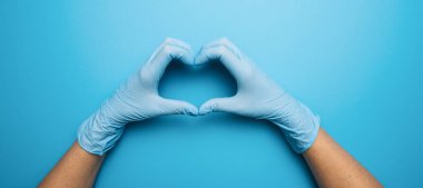 Doctor's hands in medical gloves in shape of heart on blue background, banner size, with copyspace for your individual text.