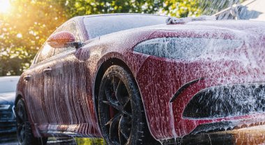 Spraying foam to a red car with high pressure foam gun car wash at car wash service