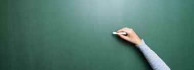 Blank blackboard / chalkboard, hand writing on green chalk board holding chalk, with copyspace for your individual text.