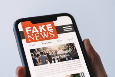 Online fake news on a mobile phone. Close up of woman reading Fake news HOAX or articles in a smartphone screen application. Hand holding smart device. Mockup website. Fake Newspaper portal.