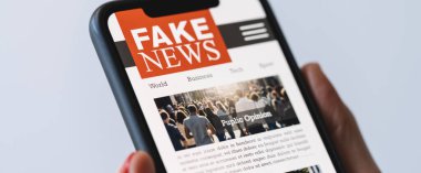 Online fake news on a mobile phone. Close up of woman reading Fake news HOAX or articles in a smartphone screen application. Hand holding smart device. Mockup website. Fake Newspaper portal.