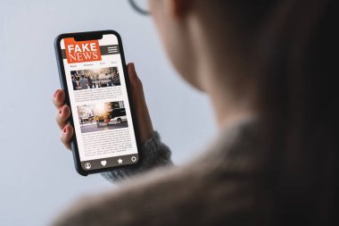 Online fake news on a mobile phone. Close up of woman reading Fake news HOAX or articles in a smartphone screen application. Hand holding smart device. Mockup website. Fake Newspaper portal.