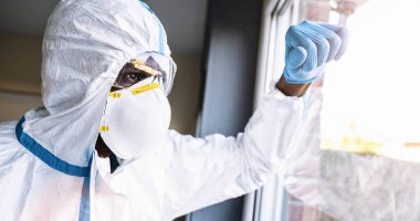 Covid-19 coronavirus epidemic overloads caregiver in protective clothing leans against the window