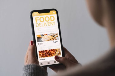 Food delivery app on a mobile phone. Restaurant order online. Woman using smartphone to get take away lunch home delivered. Fast courier service. Suhsi and Pizza menu mock up in cellphone screen.