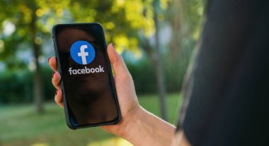 BERLİN, ALMANY AĞUSTOS 2019: Parkta Facebook uygulaması logosu olan iPhone X 'leri tutan kadın. Facebook, Mark Zuckerberg tarafından Şubat 2004 'te kurulan bir çevrimiçi sosyal ağ servisidir..