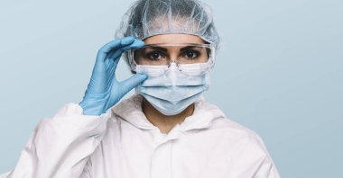 Kadın doktor ya da hemşire koruyucu eldiven ve tıbbi koruyucu maske takıyor ve yüzüne gözlük takıyor. Coronavirus COVID-19 için koruma