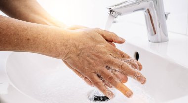 Evde banyo lavabosunda ellerini sabun ve sıcak suyla yıkayan yaşlı kadın Coronavirus salgınını önlemek için el hijyenini temizliyor. Corona Virüsü sık sık ellerini yıkayarak salgın hastalıktan korunuyor..
