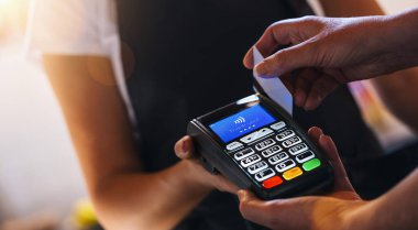 Garson, müşteri kartlarını okşarken kredi kartı makinesini tutuyor. Kafeteryada kredi kartıyla ödeme yapan bir kadın. Müşteri kahvesini ve kahvaltısını kredi kartı okuyucusuyla ödüyor..