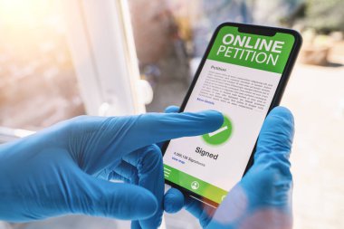 Online Dilekçe, cep telefonundan. Bakıcının kapattığı online dilekçe akıllı telefon ekran uygulaması ile imzalanmış. El ele tutuşan akıllı cihaz. Covid-19 Coronavirus salgınının web sitesi 