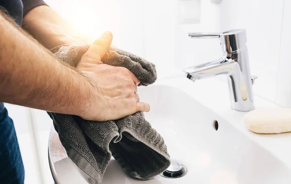 dry hands man use towel after washing hands at sink, Coronavirus 2019-ncov prevention hand hygiene. Corona Virus pandemic protection by cleaning hands frequently.