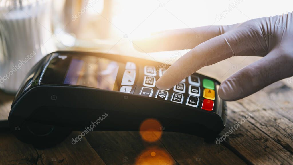 Woman hand with medical latex protective gloves enters PIN code on payment terminal in a bar. Protection for Coronavirus COVID-19. 