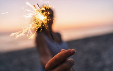 Genç bir kadın gün batımında maytapla sahilde duruyor.