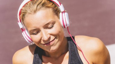 Fitness motivasyonu için kulaklıkla müzik dinleyen genç bir kadın. Spor kıyafetleri içinde oturmuş ilham alan genç bir kadının portresi..