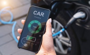 Telefondan Uygulamaya Bakan Kadın Kablo ile Elektrikli Araba Yüklüyor. Akıllı telefon ekranını kapat. El ele tutuşan akıllı cihaz. Çevre taşımacılığı için mobil uygulama. 