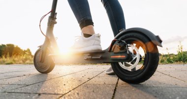 Genç kadın, şehir merkezini gün batımında elektrikli scooterla ya da e-scooterla, kentsel ulaşım konseptiyle keşfetmeye hazır.