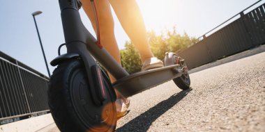 Genç bir kadın bir yaz günü elektrikli scooterla veya elektronik scooterla, kentsel ulaşım konsepti imajıyla şehir merkezini keşfetmeye hazır.