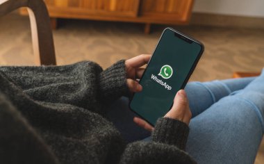 BERLİN, ALMANY AĞUSTOS 2019: Bir oturma odasında Whatsapp uygulamasını açan iPhone X 'leri tutan kadın. İnternet üzerinden mesaj göndermek için WhatsApp habercisi.