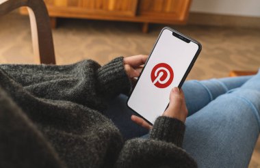 BERLİN, ALMANY AĞUSTOS 2019: Bir oturma odasında Pinterest uygulamasının logosu olan iPhone X 'leri tutan kadın. Pinterest, insanların ilginç şeylerini iğnelemesini sağlayan çevrimiçi bir pinboard..