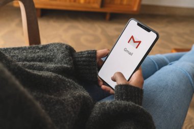 BERLIN, GERMANY AUGUST 2019: Woman holding a iPhone with Google Gmail app logo on the display. Gmail is a most popular free Internet e-mail service provided by Google. clipart