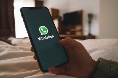 BERLİN, ALMANY AĞUSTOS 2019: Bir otel odasında Whatsapp uygulamasını açan iPhone X 'leri tutan kadın. İnternet üzerinden mesaj göndermek için WhatsApp habercisi.
