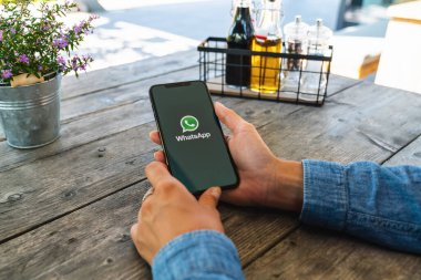 BERLİN, ALMANY HAZİRAN 2019: Bir restoranda Whatsapp uygulaması açan iPhone X 'leri olan bir kadın. İnternet üzerinden mesaj göndermek için WhatsApp habercisi.