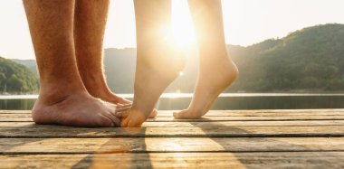 Bacakları iskelede. Gün batımında gölde sarılıp öpüşen genç bir çift. İki aşık, erkek ve kadın iskelede suyun kenarında yalınayak. Birlikte mutlu aşk anları.