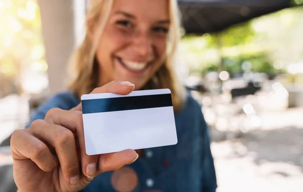 Happy young woman shows  credit card in a cafe