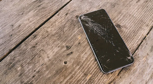 木製の背景に壊れた画面と現代の携帯電話 — ストック写真