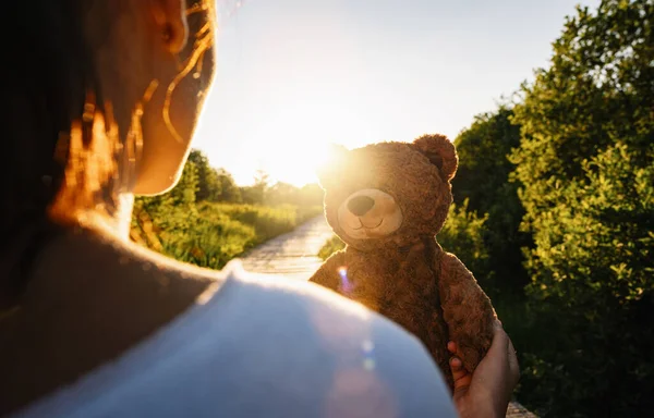 Woman holding teddy bear toy at sunset, copyspace for your individual text.