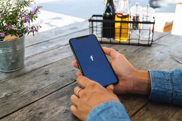 德国2019年7月 女性手持带有Facebook应用标识的Iphone Xs进入餐馆 Facebook是Mark Zuckerberg于2004年2月创立的在线社交网络服务 — 图库照片