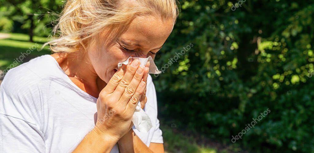 Panorama of sick or allergic woman sneezing with tissue