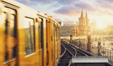 Berliner U-Bahn 'ın panoramik manzarası, Oberbaum Köprüsü' nün arka planında, gün batımında dramatik bulutlarla, Berlin Friedrichshain-Kreuzberg