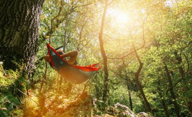 Hamakta dinlenen adam ormandaki ağaçların arasında asılı duruyor.