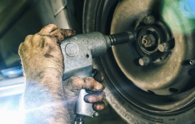 Tamirci tamirhanede araba lastiğini değiştiriyor ve cıvataları gevşetmek için elektrikli matkap kullanıyor. Tamir servisi. otantik yakın çekim 