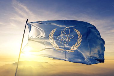 Uluslararası Atom Enerjisi Ajansı IAEA bayrağı Tekstil Kumaş kumaş üst gündoğumu sis sis üzerinde sallayarak