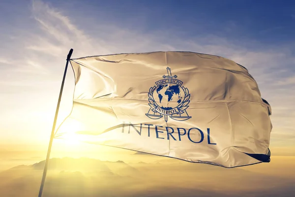 Uluslararası Ceza polis örgütü Interpol bayrak Tekstil Kumaş kumaş üst gündoğumu sis sis üzerinde sallayarak