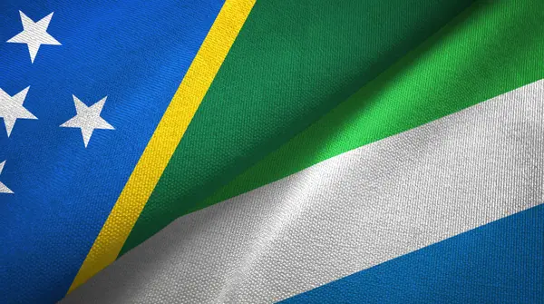 Ilhas Salomão e Serra Leoa duas bandeiras de pano têxtil, textura de tecido — Fotografia de Stock