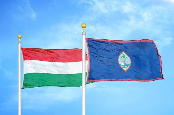 stock image Hungary and Guam two flags on flagpoles and blue cloudy sky background