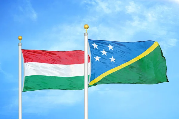 Hungary and Solomon Islands two flags on flagpoles and blue cloudy sky background