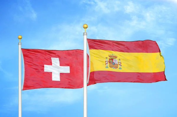 Switzerland and Spain two flags on flagpoles and blue cloudy sky background