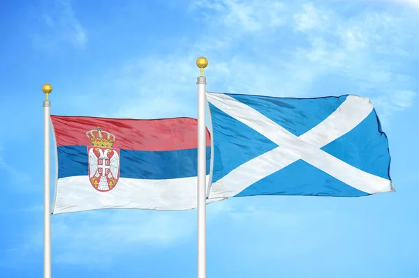 Serbia and Scotland two flags on flagpoles and blue cloudy sky background